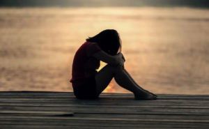 Κοπέλα στέκεται μπροστά από τη θάλασσα προβληματισμένη